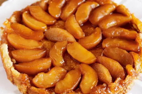 En gyllene tarte tatin med karamelliserade äppelklyftor som glänser. En klassisk fransk dessert som ser utsökt ut.