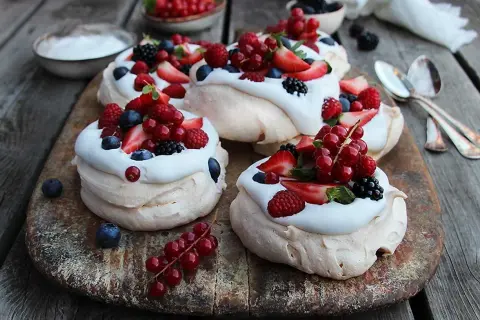 Små pavlova med grädde och färska bär som jordgubbar, hallon, blåbär och vinbär. En härlig sommardessert.