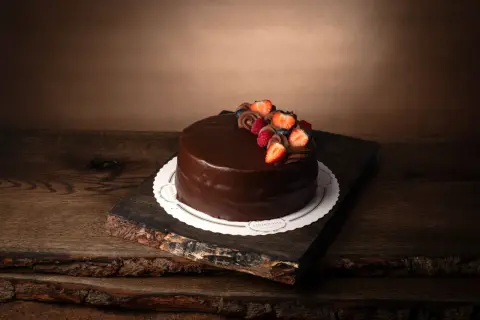 En lyxig fransk chokladtårta med färska bär och chokladdekorationer, serverad på en rustik träbricka.
