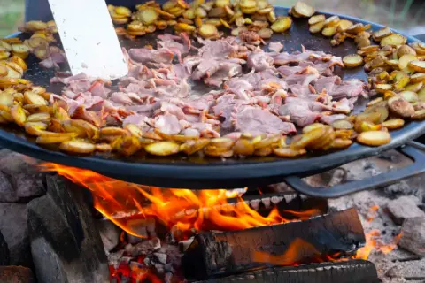 Kött och potatis steks på en Muurikka över öppen eld. Ett perfekt recept för utomhusmatlagning.