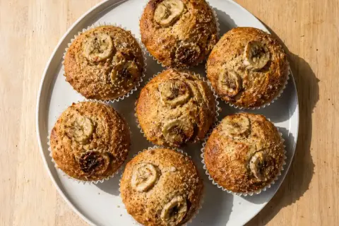 Sju gyllene bananmuffins med skivor av banan på toppen, redo att avnjutas. Ett perfekt bananmuffins recept för fika.