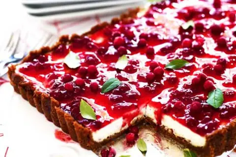 En rektangulär pepparkakscheesecake med en glansig lingonfyllning och färska lingon. Garnerad med gröna blad.