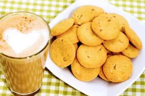 En kopp kaffe med hjärtformad lattekonst bredvid en hög med gyllene bondkakor. Perfekt för ett mysigt fika med detta bondkakor recept.