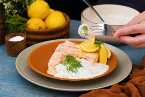 En bit lax med citron och dill, toppad med en krämig klassisk romsås. En gaffel med sås och rom lyfts från skålen.