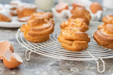 Nybakade petit choux på ett galler, med äggskal i förgrunden. Perfekt för en fika!