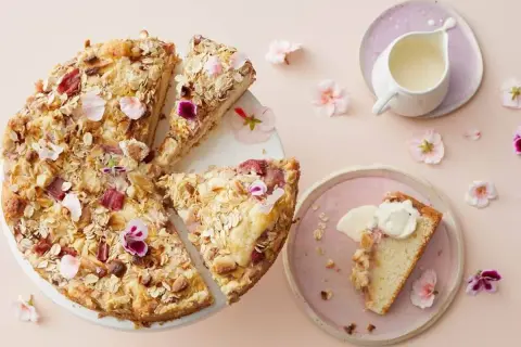 En härlig glutenfri rabarberkaka med havregryn och nötter, dekorerad med blommor. En bit serveras med grädde.