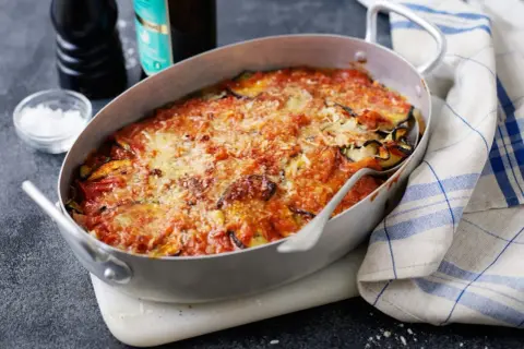 En ugnsform med en gyllene, bubblande melanzane alla parmigiana, toppad med riven ost och tomatsås. En klassisk italiensk rätt som doftar ljuvligt.
