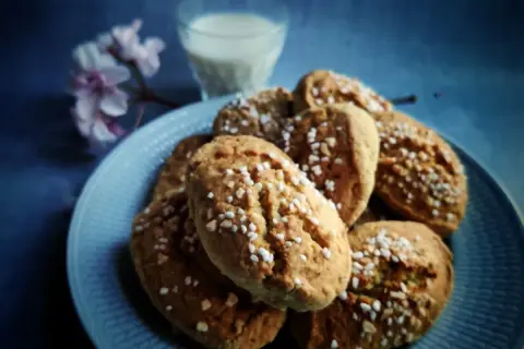 En tallrik med mandelkubbar, toppade med pärlsocker, bredvid ett glas mjölk och en blommande kvist. Perfekt för ett mandelkubb recept.