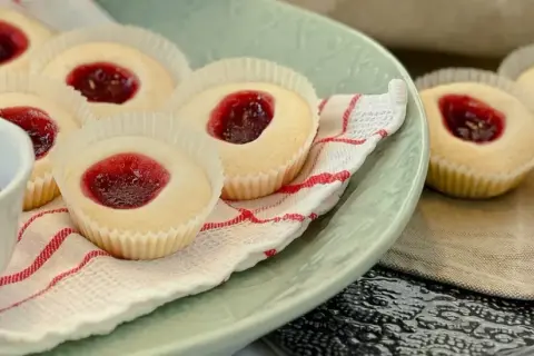 Glutenfria hallongrottor med sylt på en ljusgrön tallrik, bredvid en skål med hallonsylt och en sked.