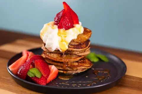 En stapel bananpannkakor med vispgrädde, jordgubbar och sirap. Ett perfekt bananpannkaka recept för frukost eller brunch.