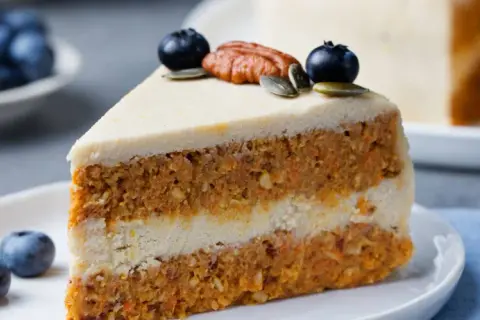 En saftig bit vegansk morotskaka med krämig frosting, toppad med blåbär och pekannöt. En härlig fika!