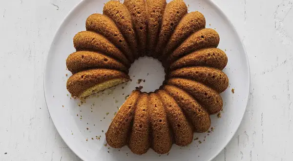 En gyllene sockerkaka med kardemumma, med en bit borttagen, ligger på en vit tallrik.