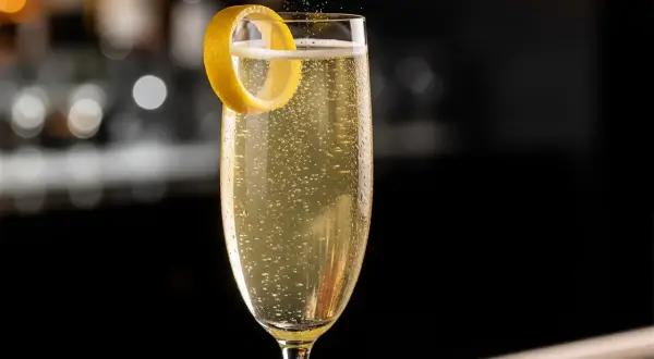 Ett glas French 75 med bubblor och en citronskal.