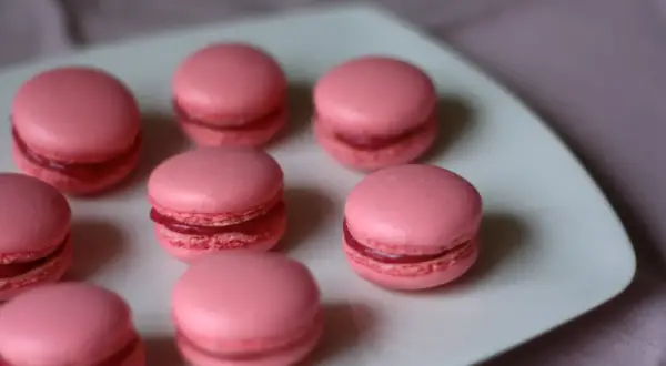 Rosa macarons med fyllning på en vit tallrik. Perfekt för ett macarons recept.