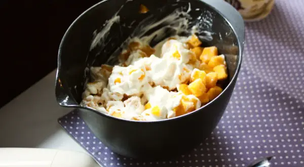 En skål med fruktbitar och krämig kvarg, redo att bli en härlig kvarg glass. En stavmixer ligger bredvid.