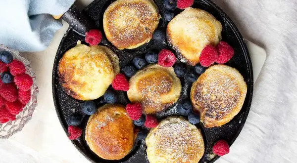 Små, gyllene pannkakor med pudersocker och bär, redo att avnjutas. Ett perfekt krabbelurer recept för frukost eller fika.