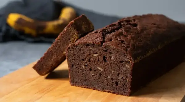 En saftig banankaka i sockerkaksform, med en skiva upplagd. En övermogen banan ligger i bakgrunden.