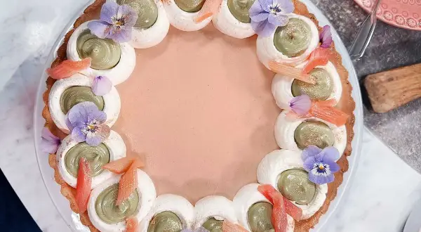 En vacker pannacotta med rabarber, dekorerad med grön kräm, maräng, violer och rabarberbitar.