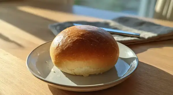 En gyllene, luftig semla på en tallrik, redo att fyllas med grädde och mandelmassa. Solen lyser in genom fönstret.