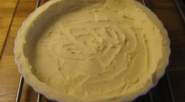 En ljusgul, krämig glutenfri pajdeg i en vit pajform, redo att fyllas.