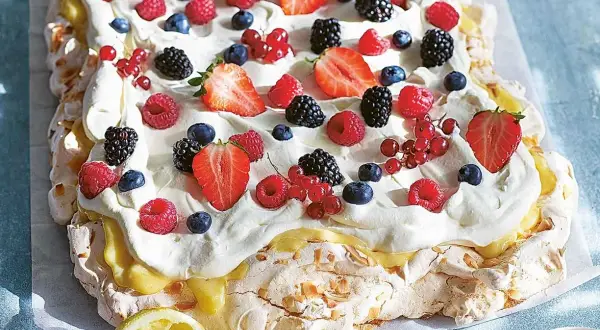 En stor pavlova med lemoncurd, toppad med vispgrädde och färska bär som jordgubbar, hallon, blåbär och vinbär.