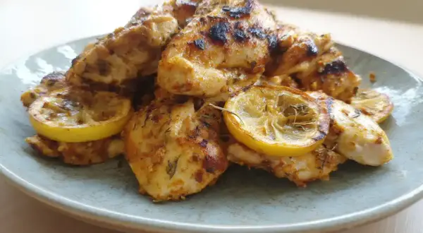 Grillad marinad kyckling med citronskivor på en ljusblå tallrik.