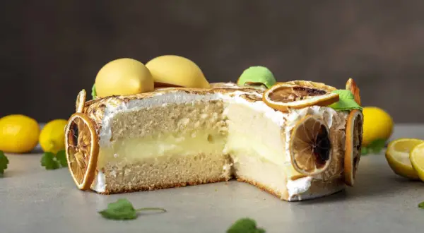 En skivad citron tarte med fluffig maräng, krämig fyllning och dekorerad med torkade citronskivor och gula marängkulor.