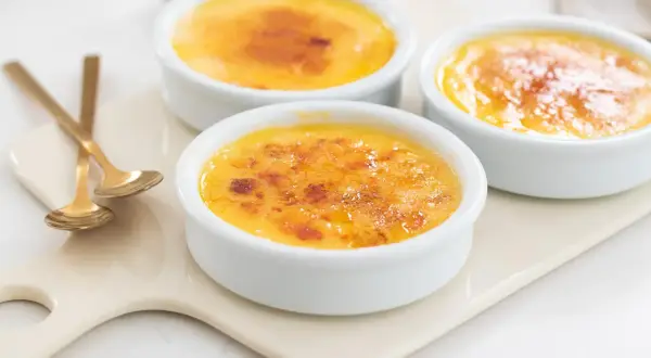 Tre krämiga crème brûlée i vita skålar med karamelliserat socker. Perfekt för ett enkelt creme brulee recept.