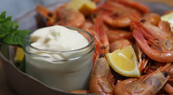 En skål med räkor och citronklyftor, med en liten burk krämig aioli. Perfekt för ett enkelt aioli recept.