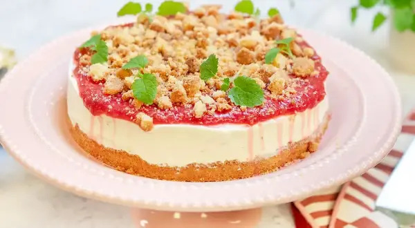 En läcker rabarber cheesecake med smulig topping och myntablad, serverad på ett rosa tårtfat.