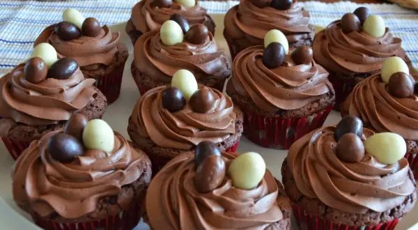 En bricka med chokladmuffins med krämig choklad frosting, dekorerade med små chokladägg i olika färger.