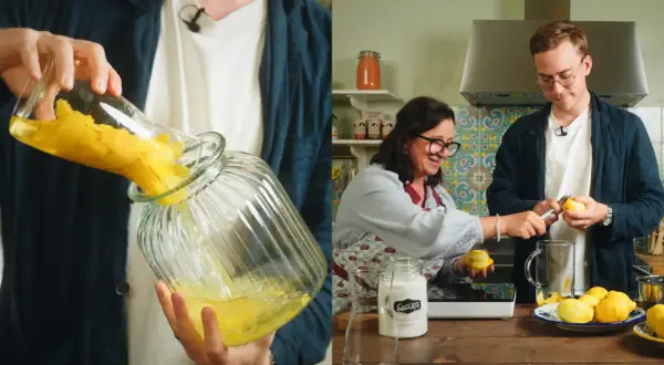 Två personer förbereder egen limoncello i ett kök. En häller citroner i en glasburk, medan den andra skalar citroner.