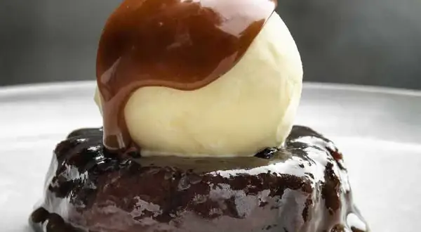 En läcker sticky toffee pudding med en kula vaniljglass och varm kolasås som rinner över.