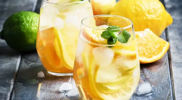 Två glas med uppfriskande vit sangria cava fyllda med frukt och is. Citroner, apelsiner och mynta ger en härlig sommarkänsla.