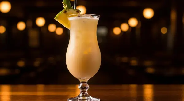 En krämig alkoholfri pina colada med ananasskiva och blad som dekoration, serverad i ett elegant glas på en träyta.
