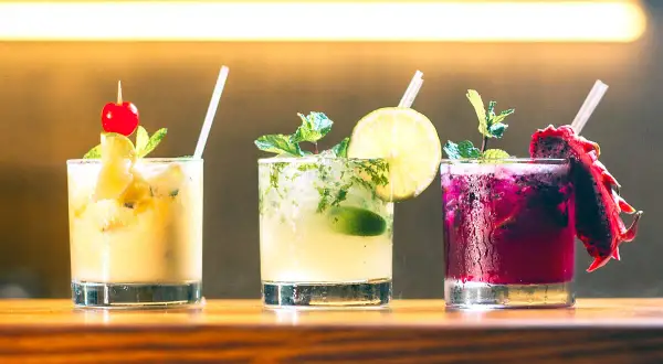 Tre färgglada alkoholfria drinkar med frukt och mynta på en träbar.