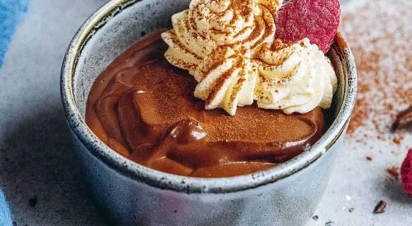 En krämig chokladpudding i en skål, toppad med vispad grädde, hallon och kanel. Perfekt för ett chokladpudding recept.