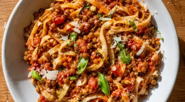 En skål med tagliatelle täckt av en mustig vegetarisk pastasås med linser, tomater och basilika, toppad med parmesan.