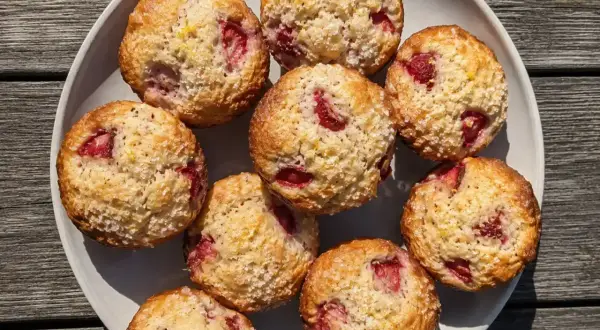 En tallrik med fluffiga muffins med jordgubbar, toppade med socker och citronskal. Perfekta för fika!