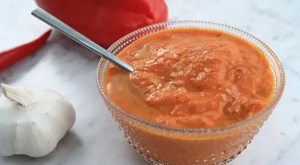 En skål med ajvar relish, en röd paprika, en chili och ett vitlökskläpp.