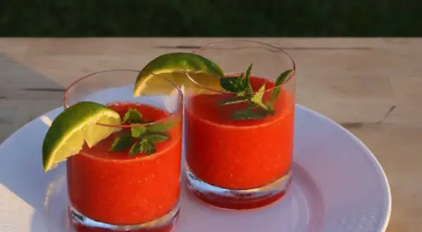 Två glas med fryst jordgubbsdaiquiri, garnerade med lime och mynta. Perfekt för ett somrigt strawberry daiquiri recept.