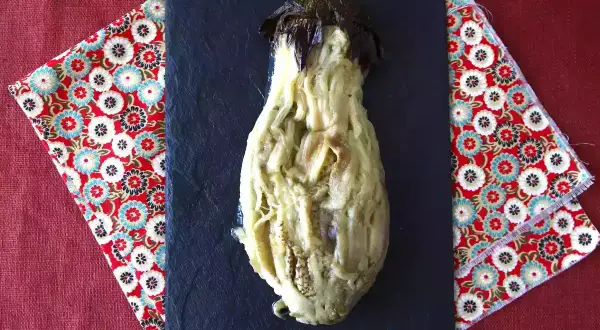 En ugnsbakad aubergine, mjuk och saftig, serveras på en svart skifferplatta.