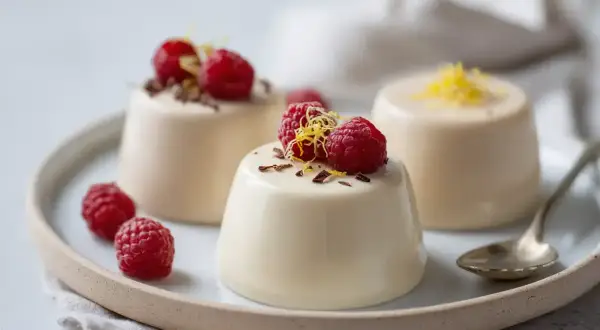 Tre krämiga panna cotta-desserter med hallon och citronskal på en tallrik.