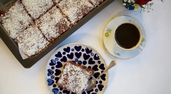 En saftig citronkaka i långpanna, toppad med kokosflingor, serveras med en kopp kaffe.