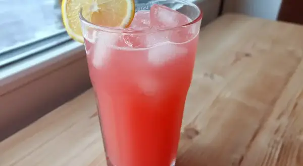 Ett glas rosa rabarberlemonad med is och en citronskiva, redo att avnjutas.