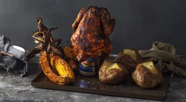 En saftig ölburkskyckling med majskolvar och bakpotatis på ett fat.
