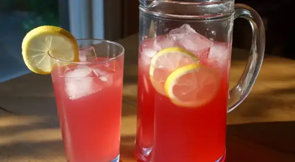 En karaff och ett glas med rosa rabarbersaft, is och citronskivor. Perfekt för ett svalkande rabarbersaft recept.