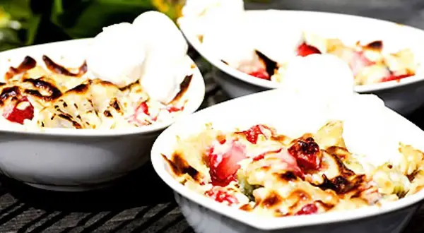 Tre skålar med jordgubbs-smulpaj toppad med vaniljglass. Ett perfekt Gino recept för en sommardessert.