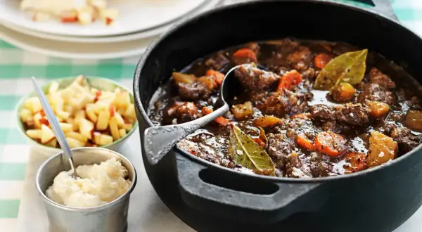 En mustig kalops med morötter och lagerblad i gjutjärnsgryta, serverad med äppelkompott och potatismos. Ett klassiskt kalops recept.