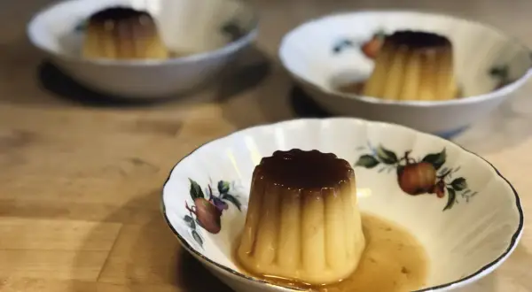 Tre krämiga creme caramel i vackra skålar med fruktmotiv. En härlig dessert som väntar.